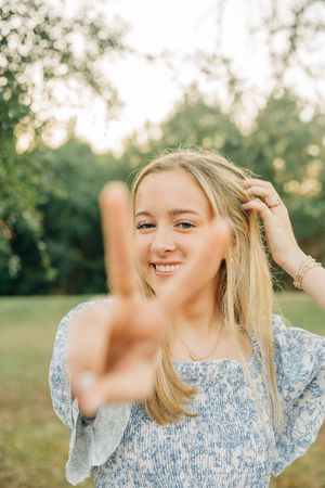 A person in a blue floral top smiles while touching their blonde hair outdoors during golden hour.
