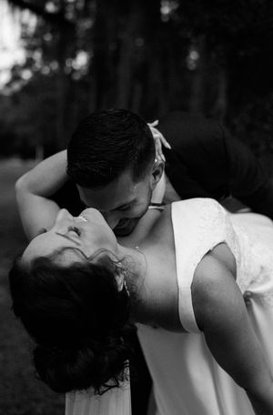 A romantic black and white wedding photo showing a couple embracing in an intimate dip pose outdoors.