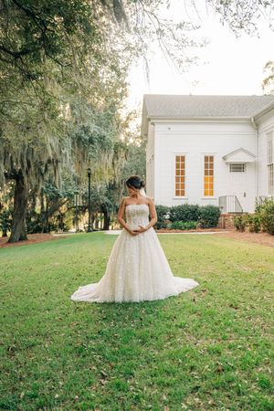 A white wedding dress photographed in a series against a rustic church backdrop with Spanish moss draped trees.