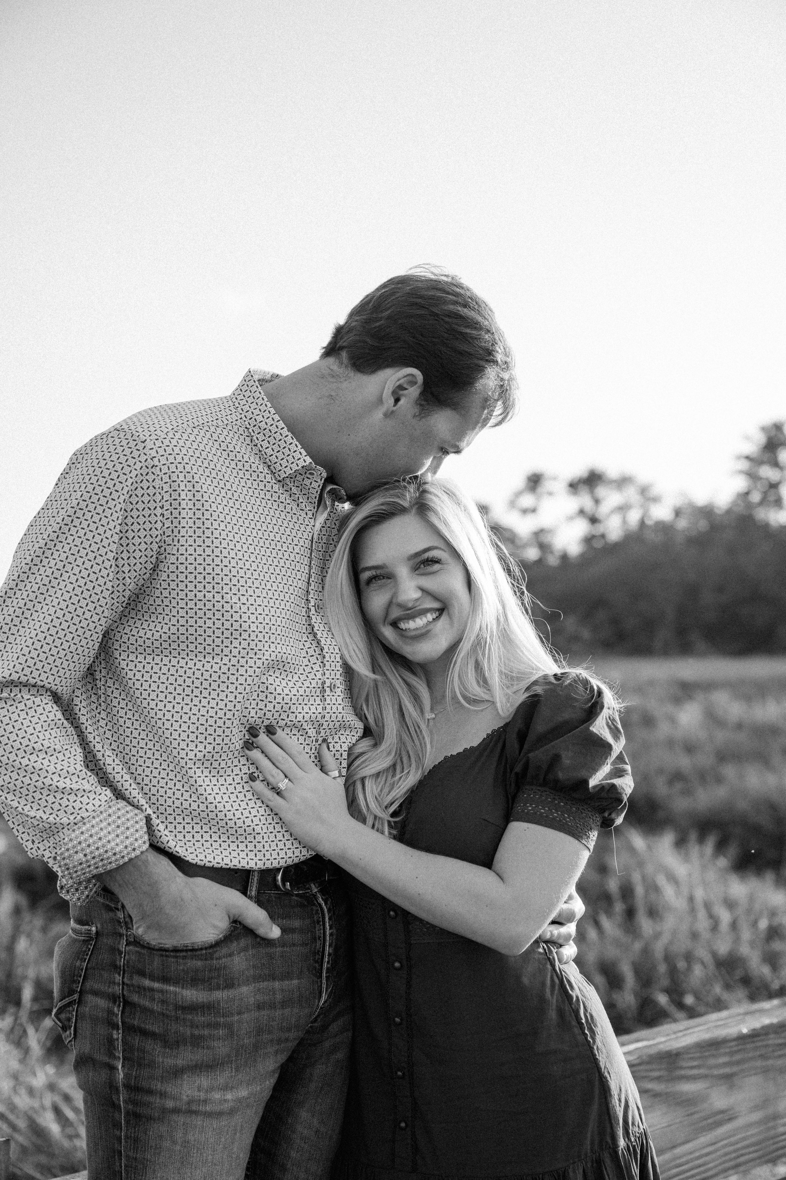 A couple shares playful candid moments together in a field during an outdoor photo session.