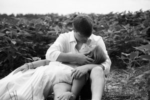 A romantic couple lies together in a grassy field on a black and white summer day.