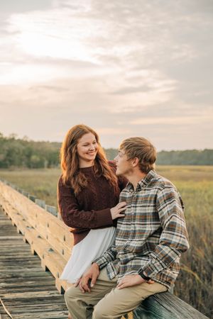 A couple shares a tender moment while sitting on a wooden boardwalk during golden hour.