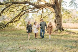 A group of people walk together beneath sprawling oak trees in a golden autumn meadow at sunset.