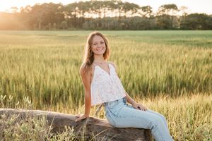 Golden sunset light illuminates a wheat field as someone poses in casual summer attire.