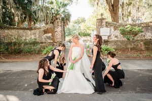 A fun wedding party photo with attendants in black dresses kneeling around a bride in white.