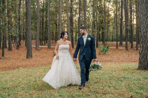 A couple in wedding attire walks together through a sunlit forest of tall pine trees on their special day.