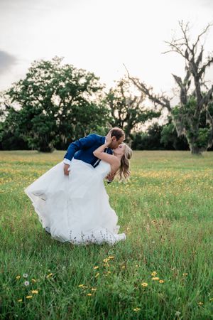 Romantic wedding couple dancing in a field of wildflowers at sunset.