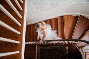 Person in white dress descending curved wooden staircase viewed from above.