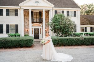 Elegant bridal portrait in front of a classic white colonial mansion with black shutters and brick accents.