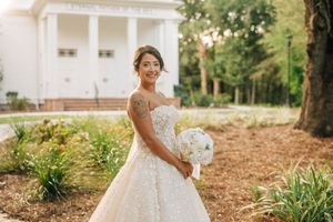 A bride in a white wedding dress poses outdoors in a garden setting with natural foliage and greenery.
