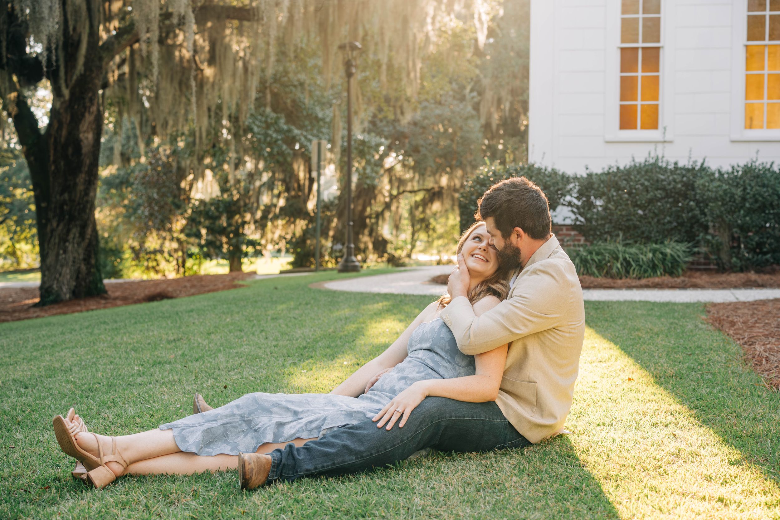 A romantic couple lounges together on grass during golden hour in a garden setting.