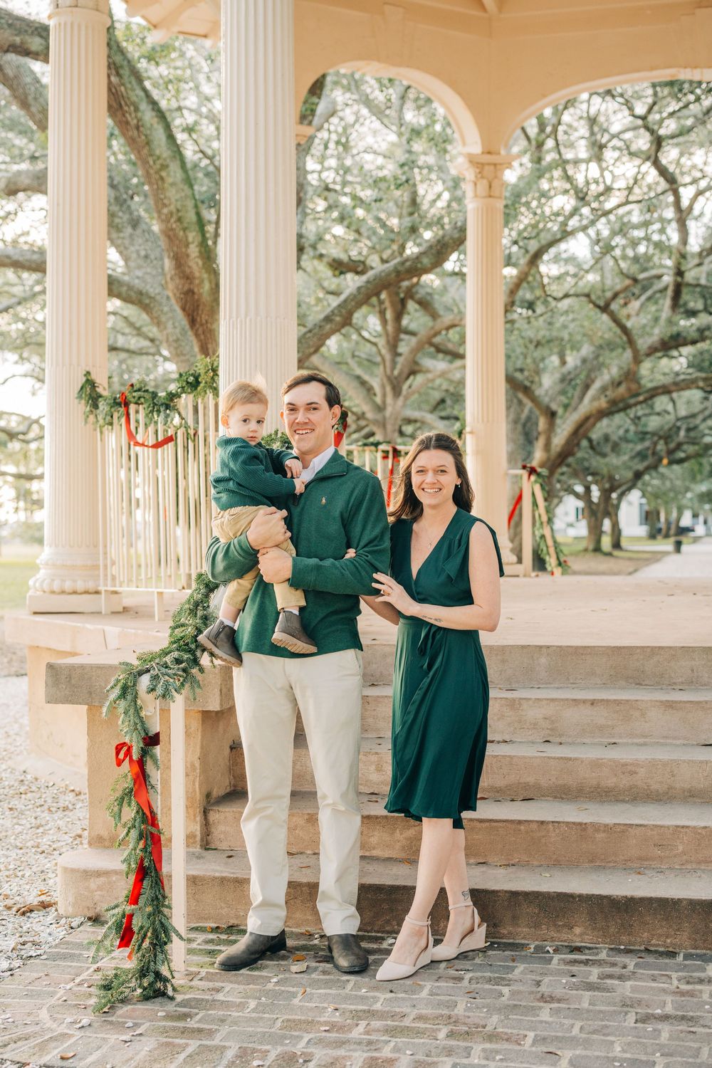 Couple in green and white attire share romantic moments under a columned gazebo surrounded by oak trees.