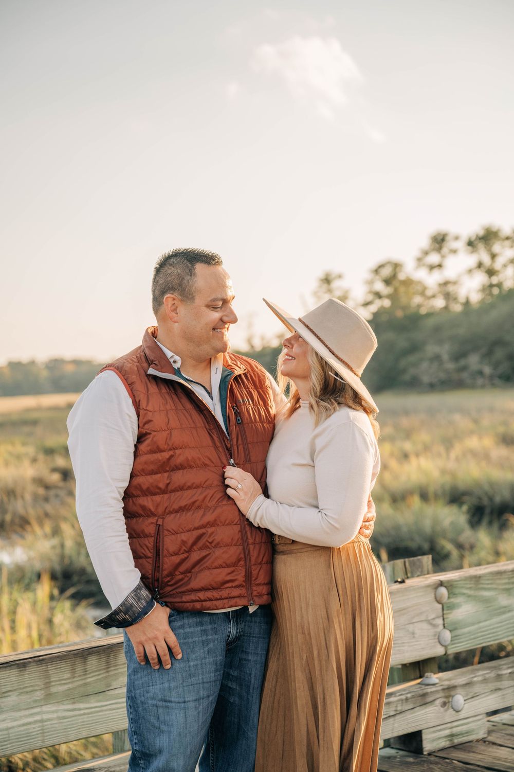 A couple shares a romantic moment on a wooden boardwalk during golden hour in a natural outdoor setting.