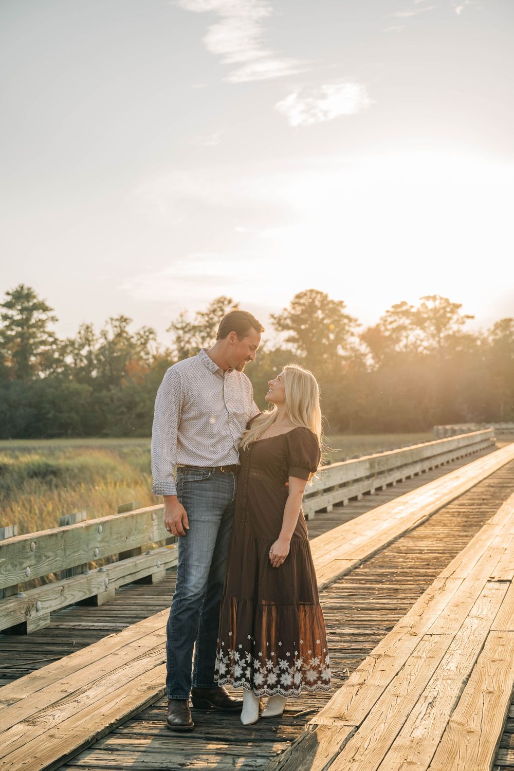 A couple shares an intimate moment on wooden train tracks at sunset with golden light filtering through trees.