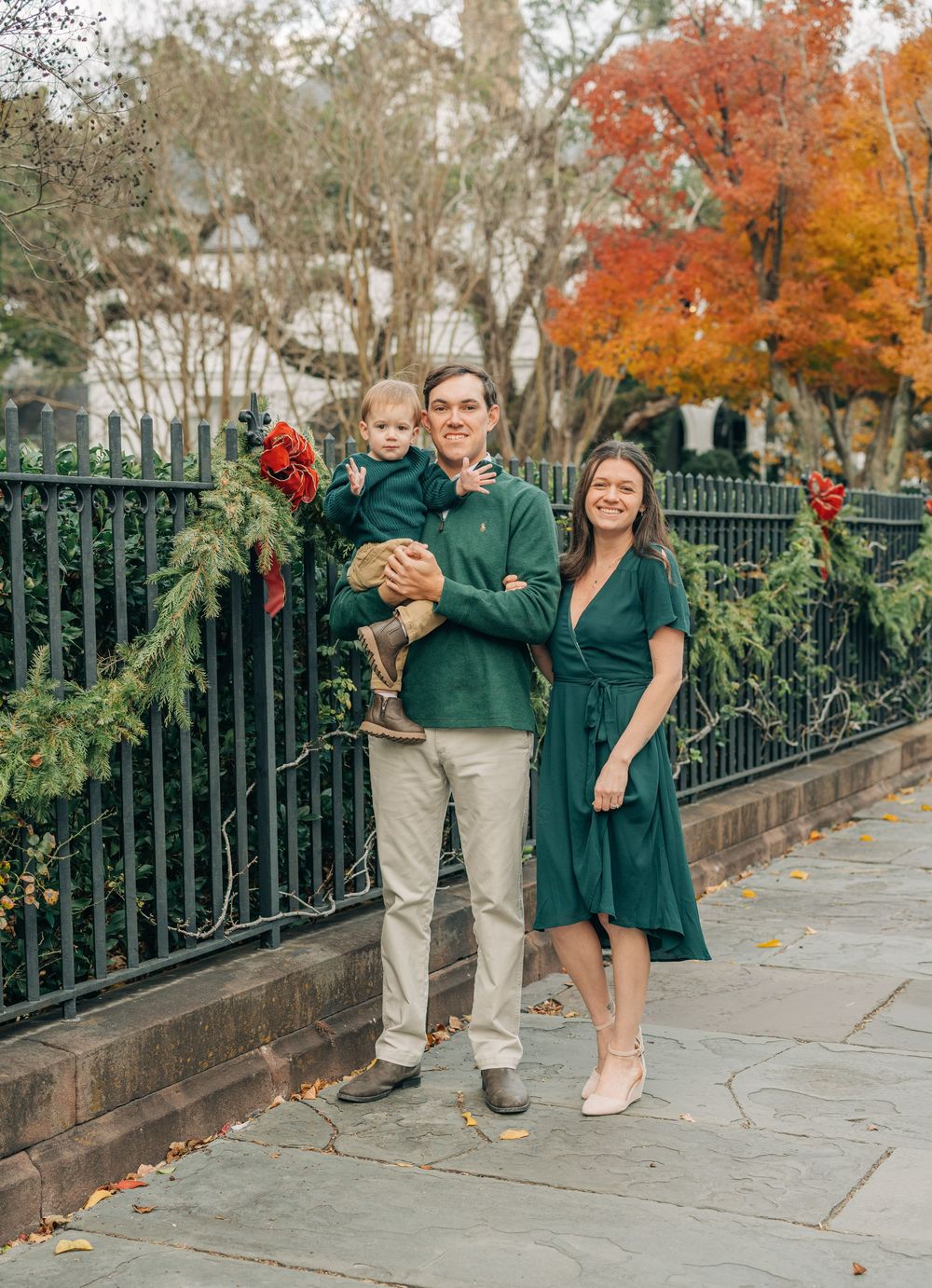 A family stands together on a stone walkway surrounded by autumn foliage and decorative iron railings.