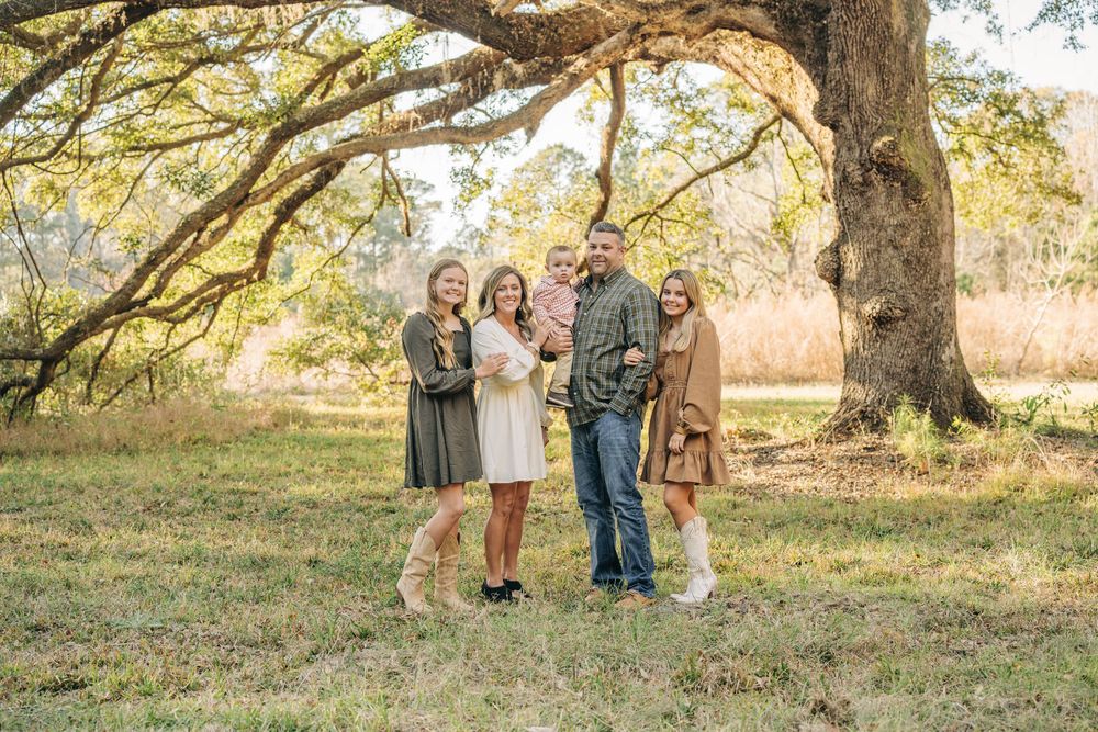 Family portraits taken outdoors under a large oak tree in a natural autumn setting during golden hour.
