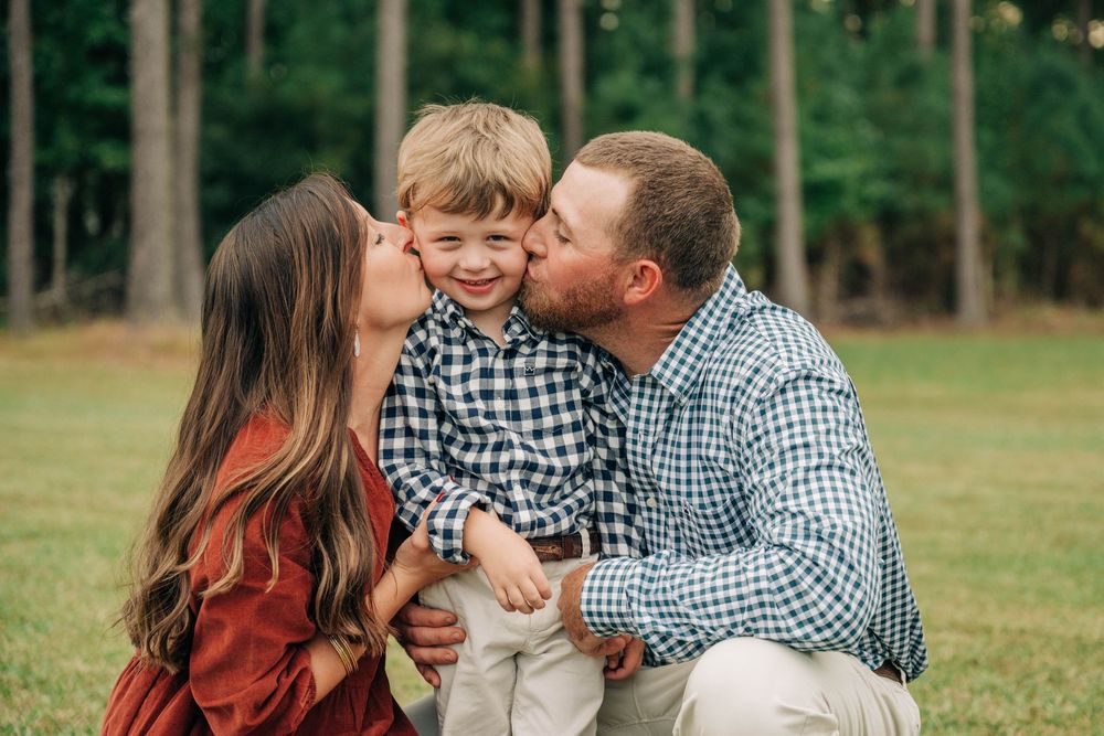 Family in coordinated outfits sharing joyful moments together during an outdoor photo session in a grassy field.