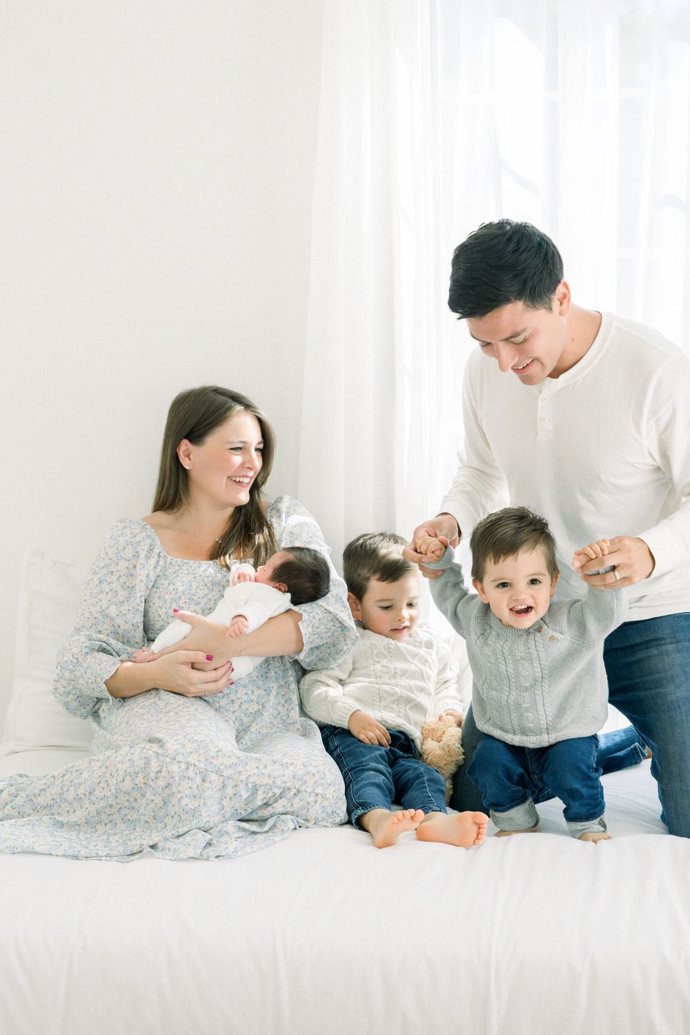 A family shares a joyful moment together on a white bed, dressed in coordinating outfits taken by a northern virginia newborn photographer