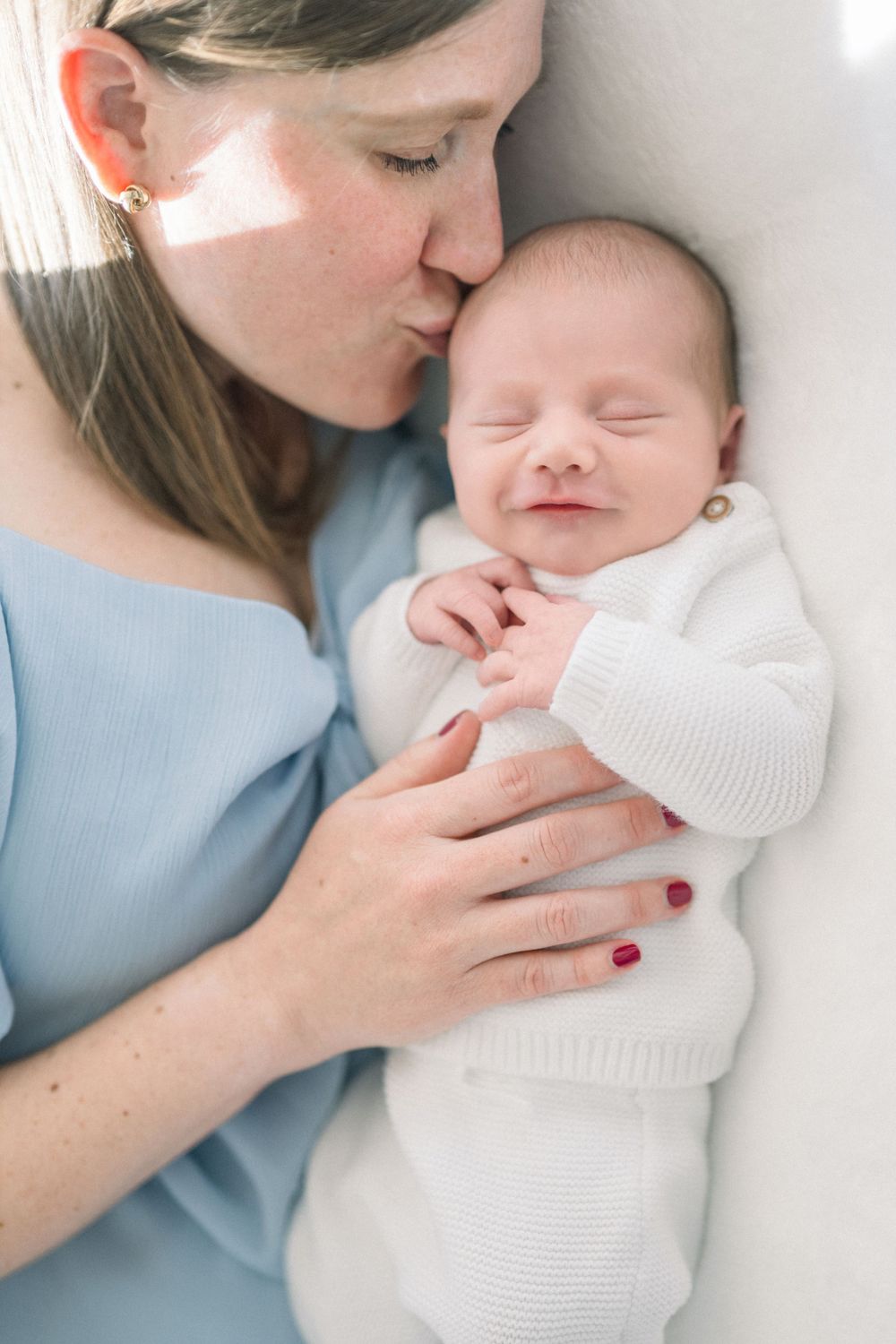 A moment between a woman in light blue and a sleeping newborn baby wrapped in white knitwear by a northern virginia newborn photographer