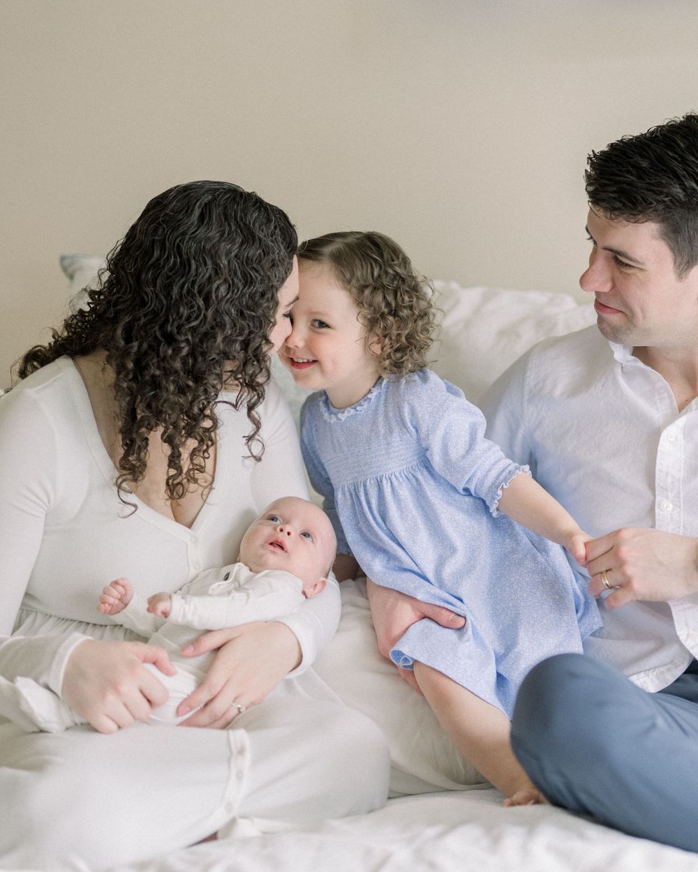 family shares a moment together lounging in white bedding while wearing light colored clothing
northern virginia newborn photographer