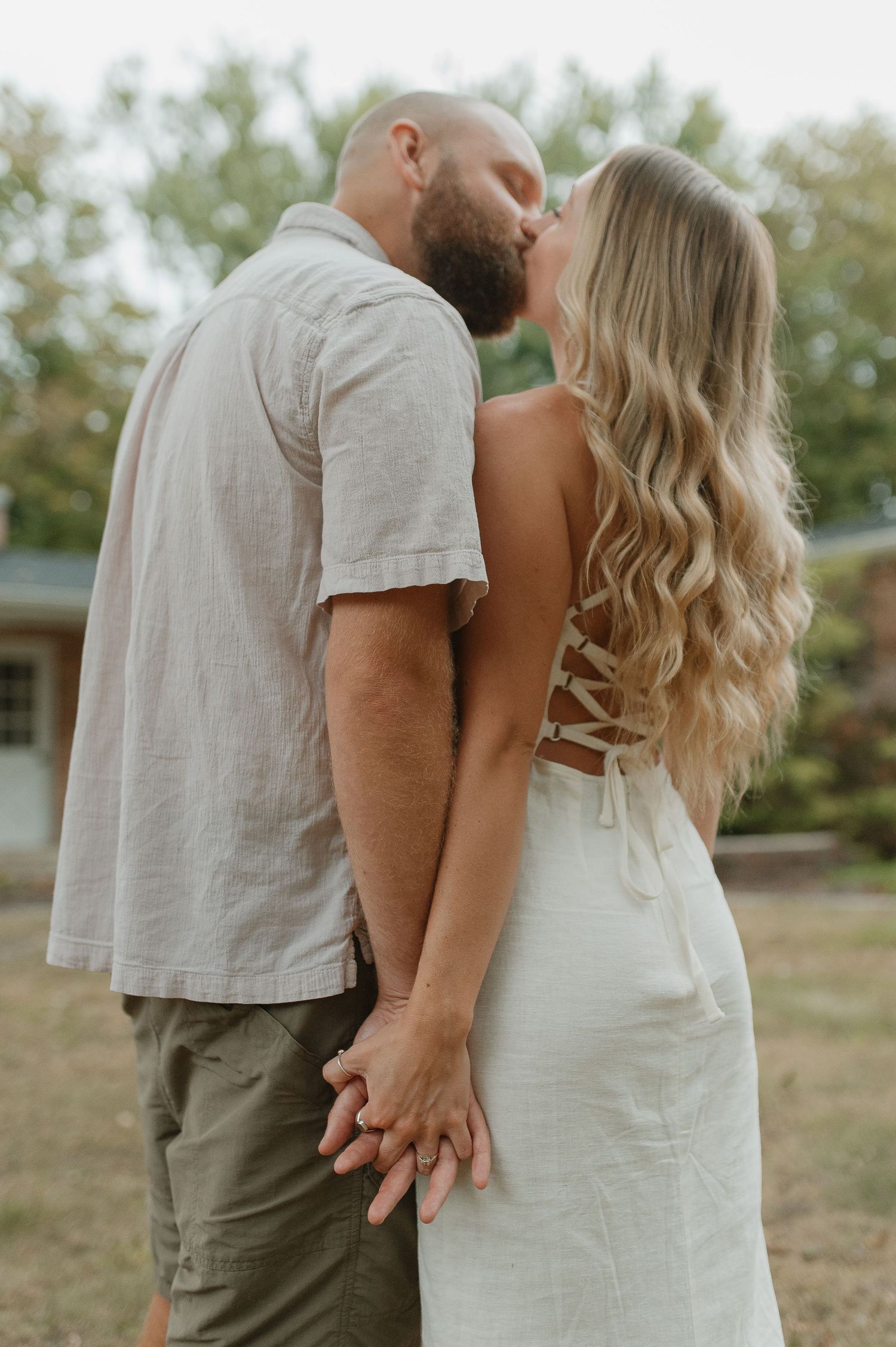 A romantic couple in light colored clothing share an intimate moment outdoors.