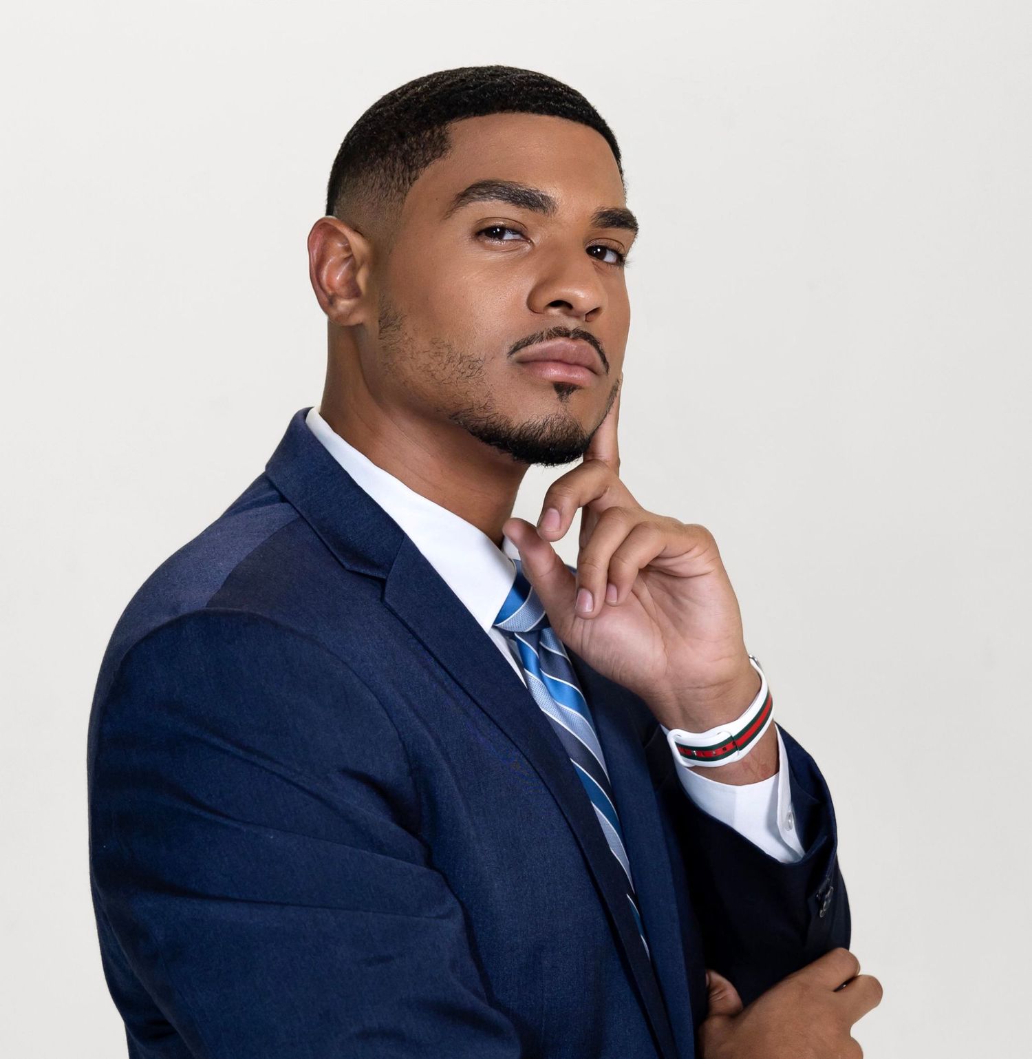 Professional headshot of person in navy suit and striped tie with thoughtful expression against white background.