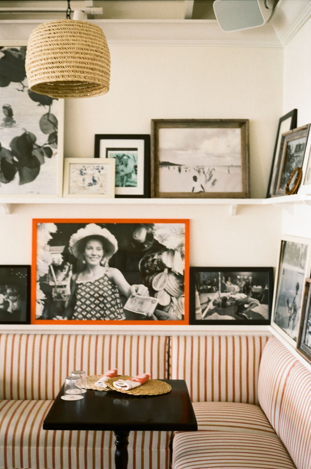 Cozy restaurant booth with orange striped upholstery, wicker pendant light, and black and white photo gallery wall.