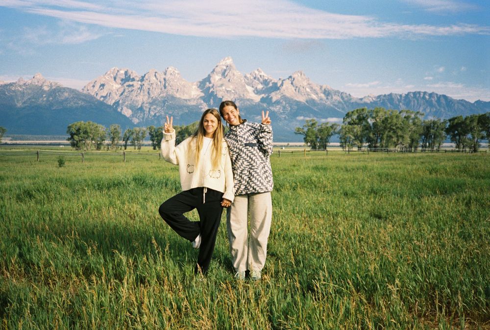 Couple posing with peace signs in a green meadow with the Grand Teton mountain range in the background.