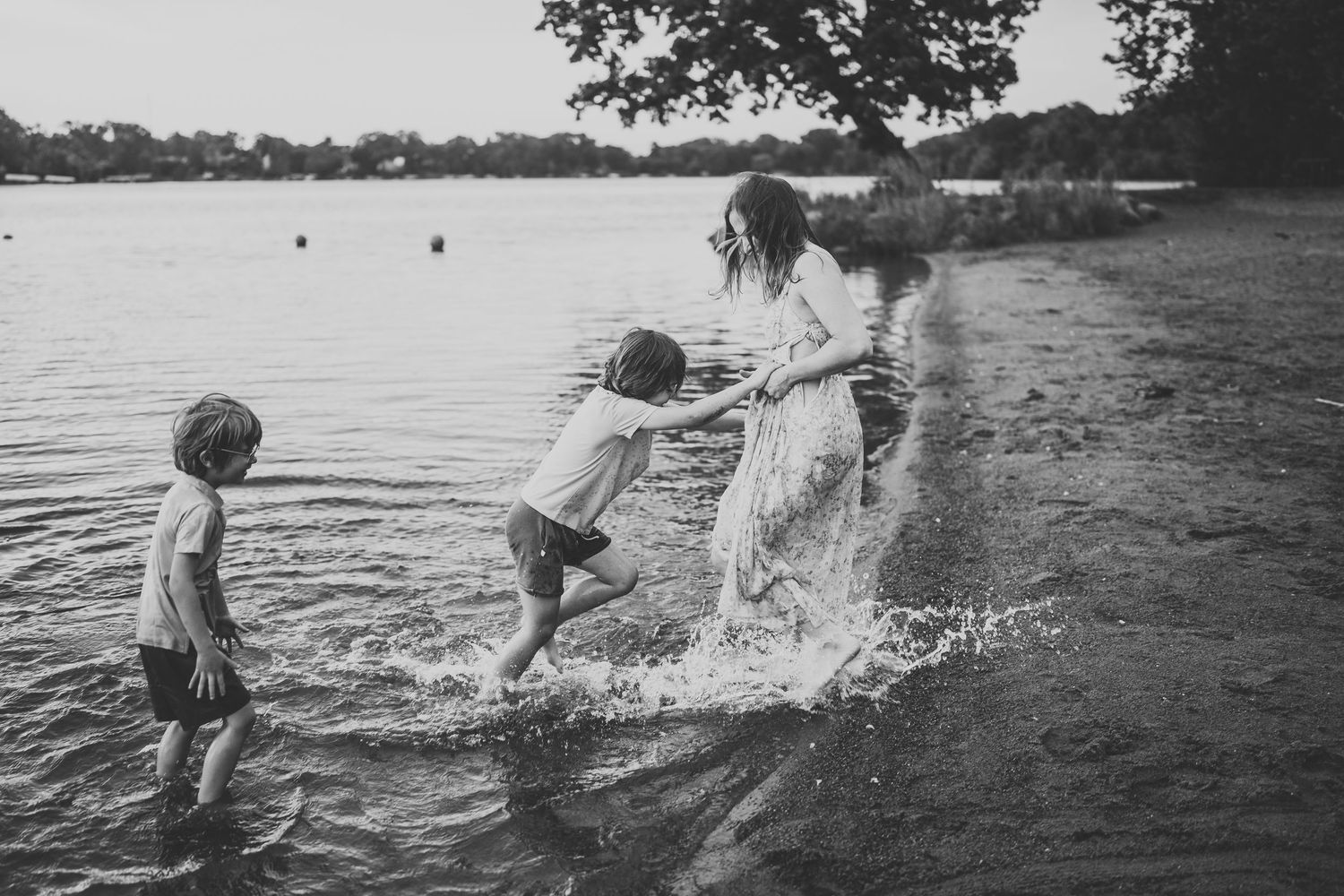 Several people splash and play in the water at a lakeside on a summer day.
