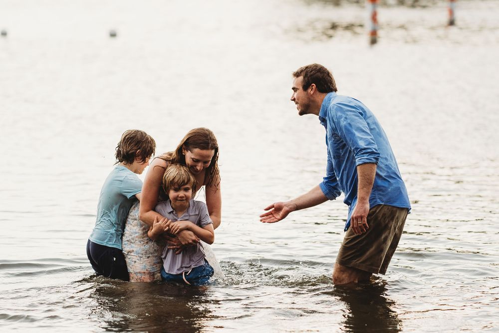 Family playing together in knee-deep lake water on a summer day.