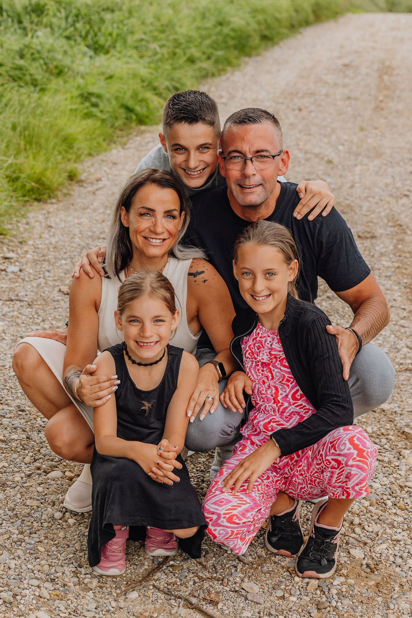 A family poses together on a dirt path surrounded by green grass on a sunny day.