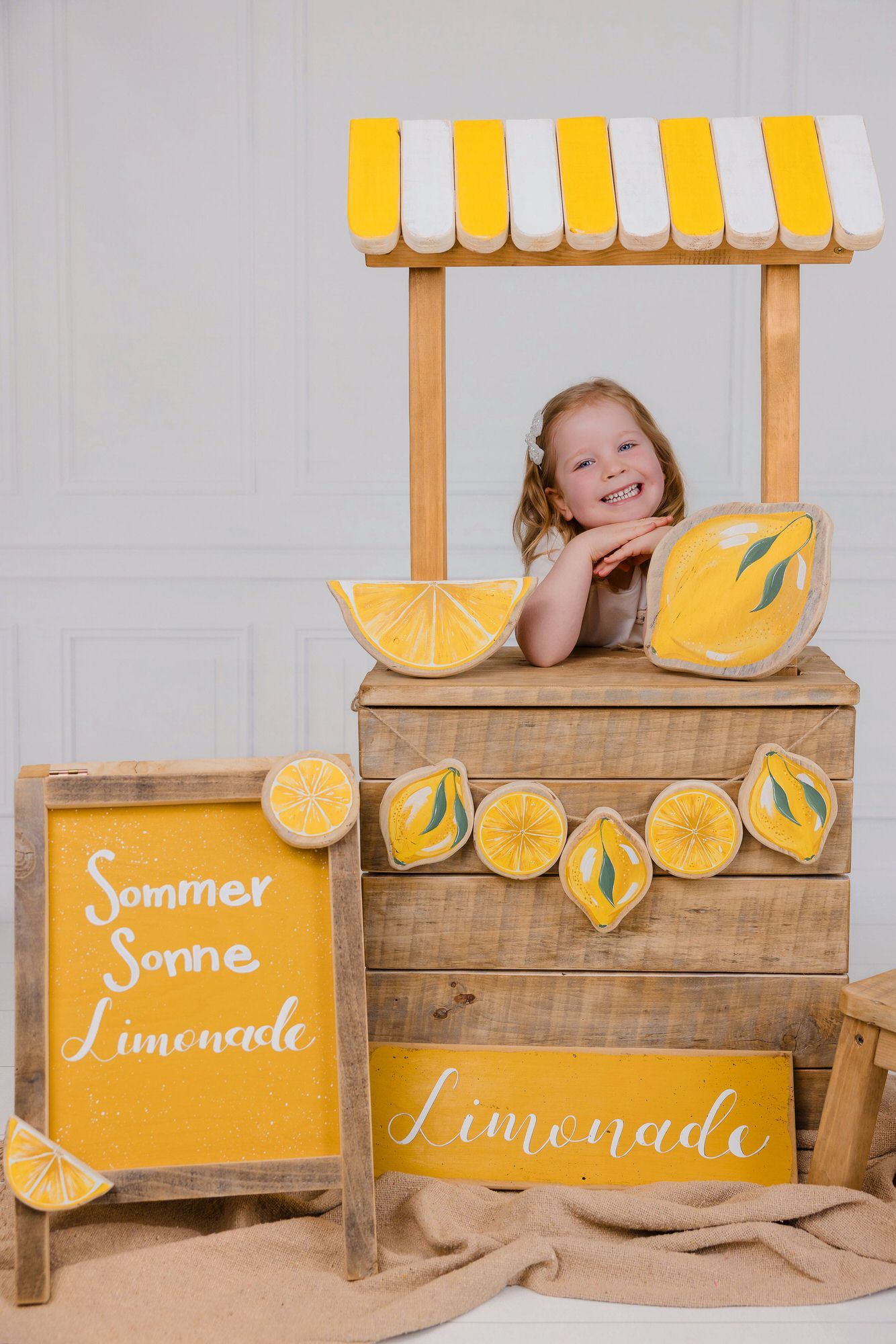 Rustic wooden lemonade stand with yellow and white striped awning and decorative painted lemons on display.