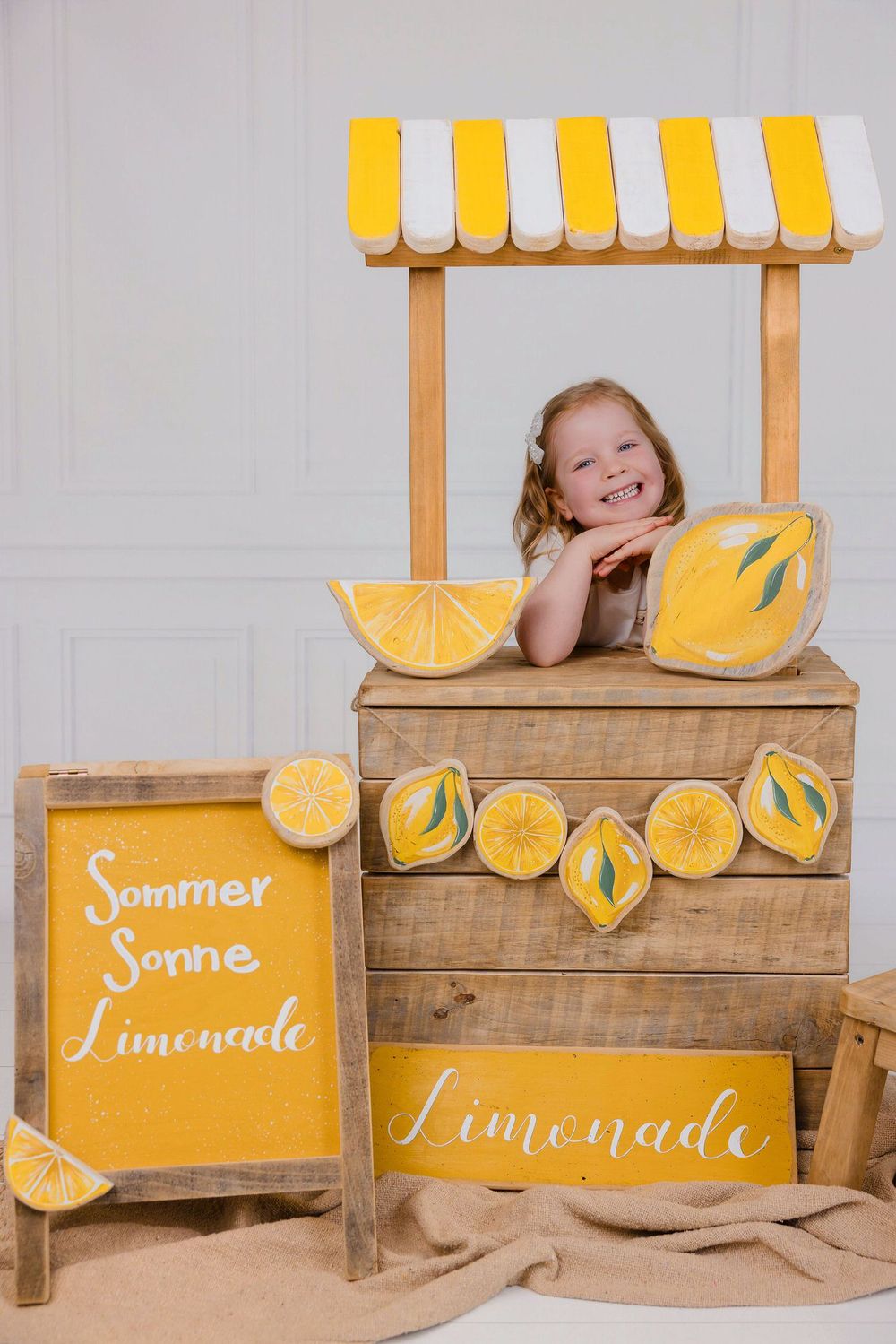 Rustic wooden lemonade stand with yellow and white striped awning and decorative painted lemons on display.
