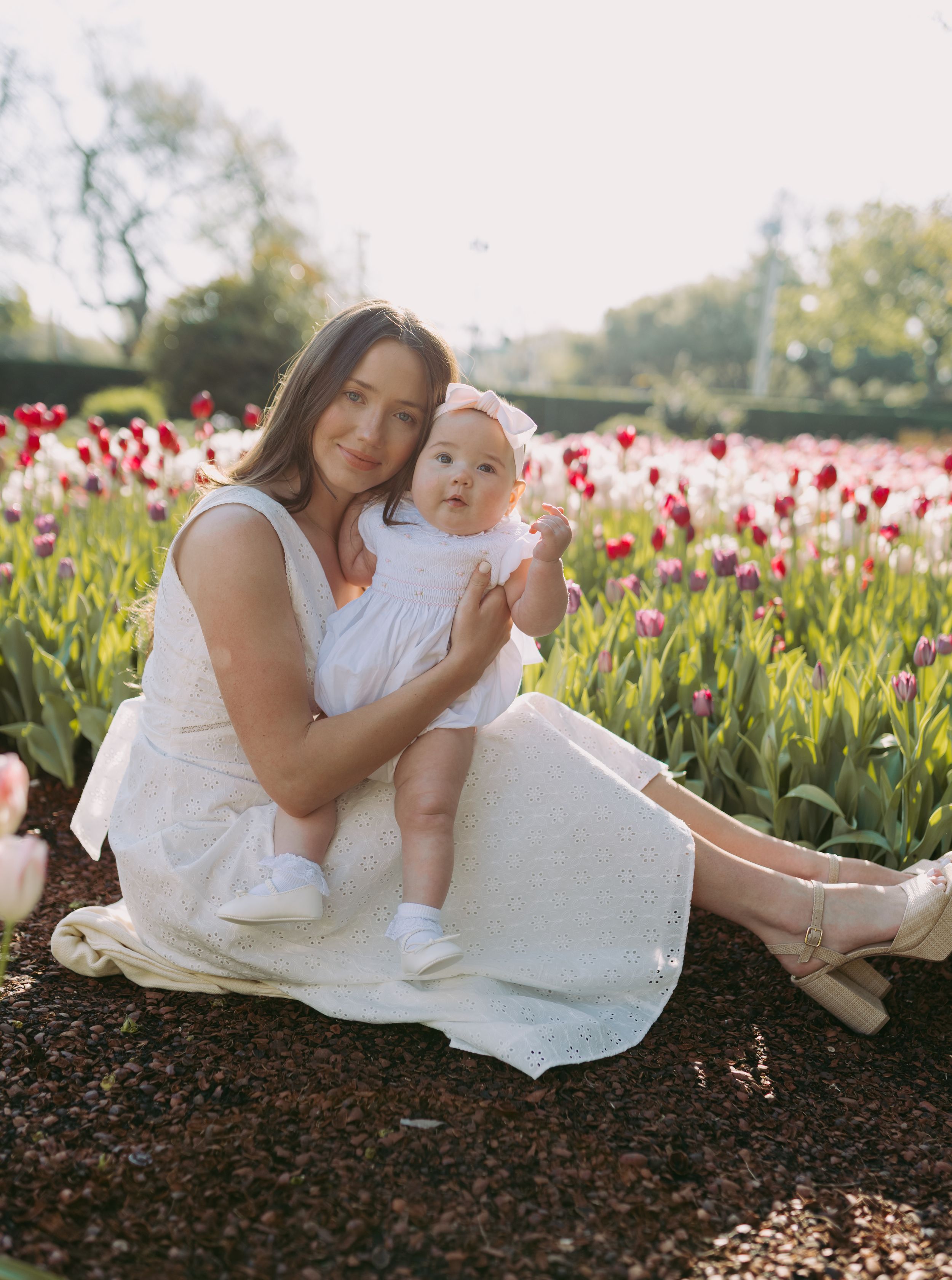 A mother and baby relax in a field of vibrant red tulips on a sunny spring day.