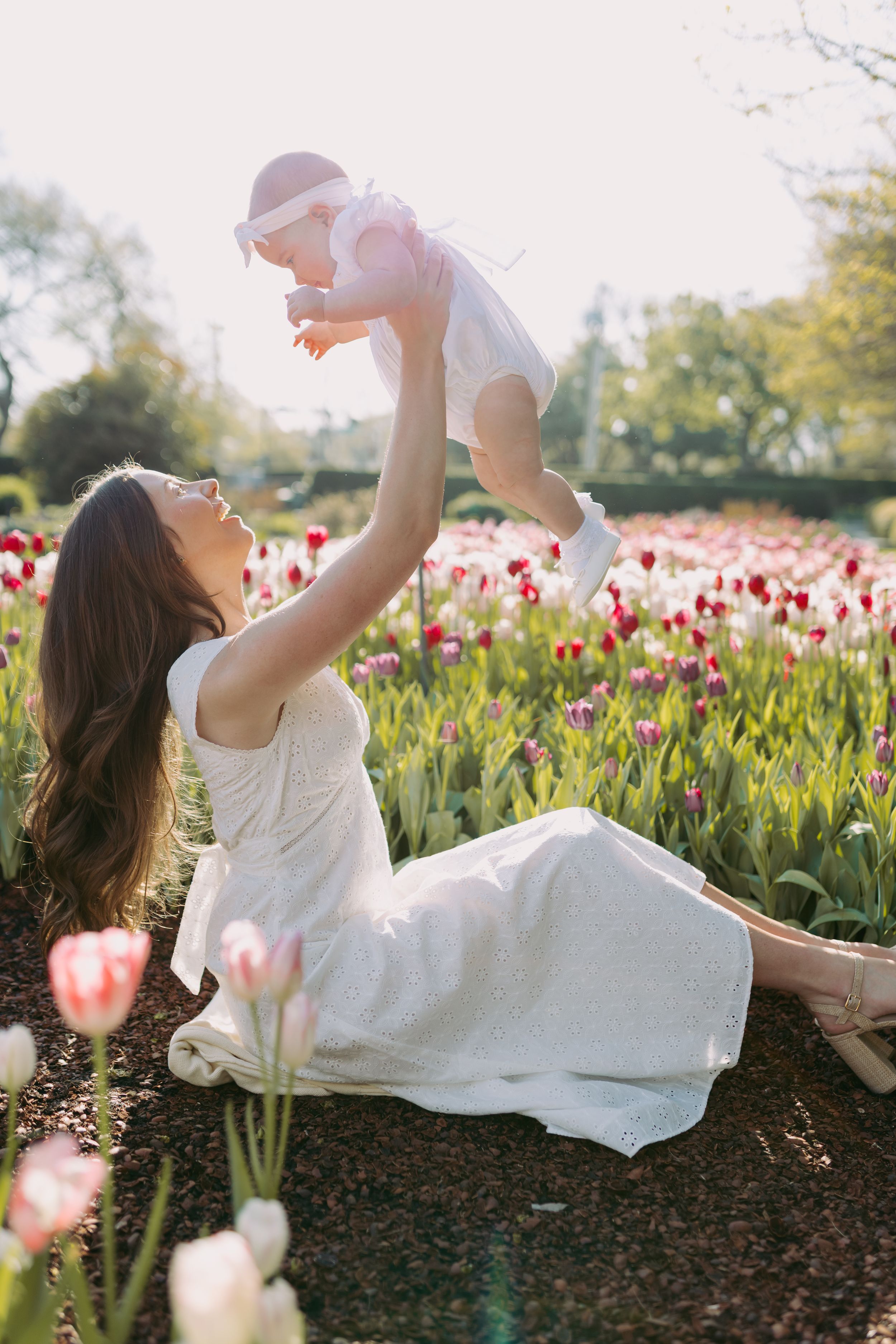 A joyful moment captured in a blooming tulip field as someone in white lifts a baby against the golden sunlight.