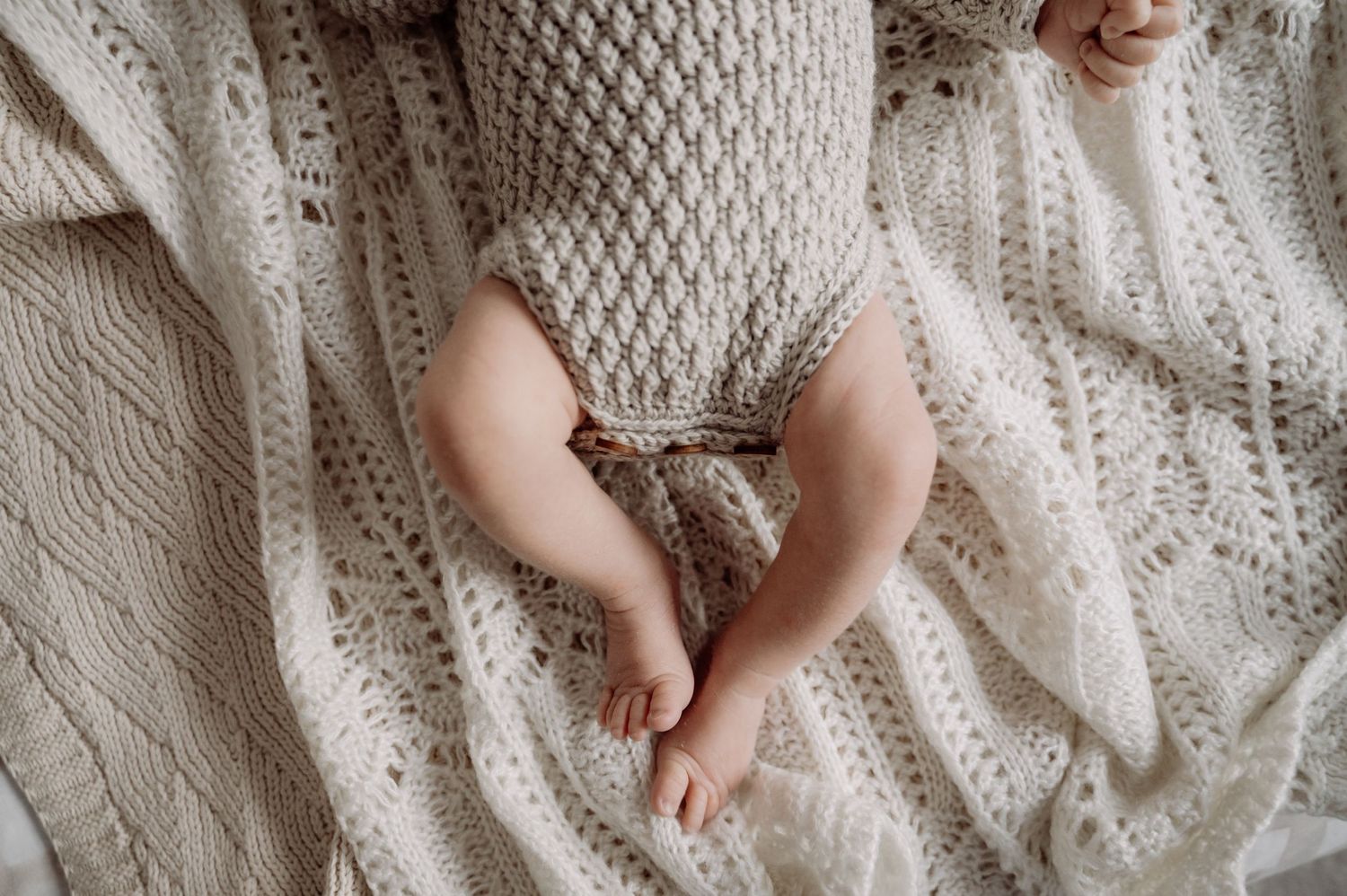 Tiny bare baby feet resting on a cozy cream-colored knit blanket with intricate cable patterns.