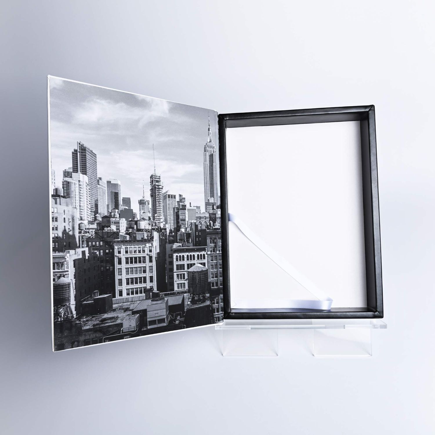 Black and white cityscape photo displayed in an open acrylic photo frame on a light gray background.