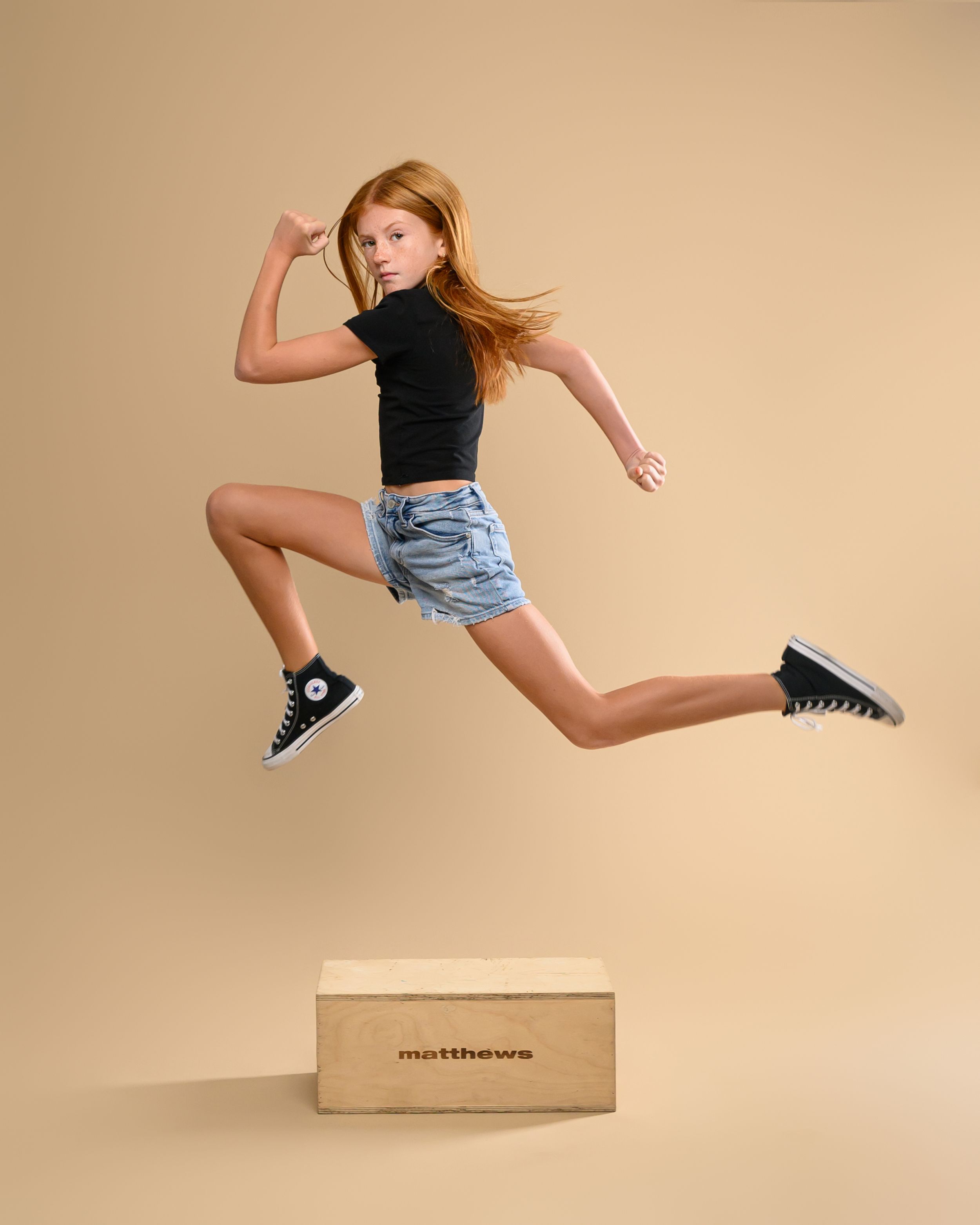 Artistic jump sequence showing movement over wooden box against beige backdrop.