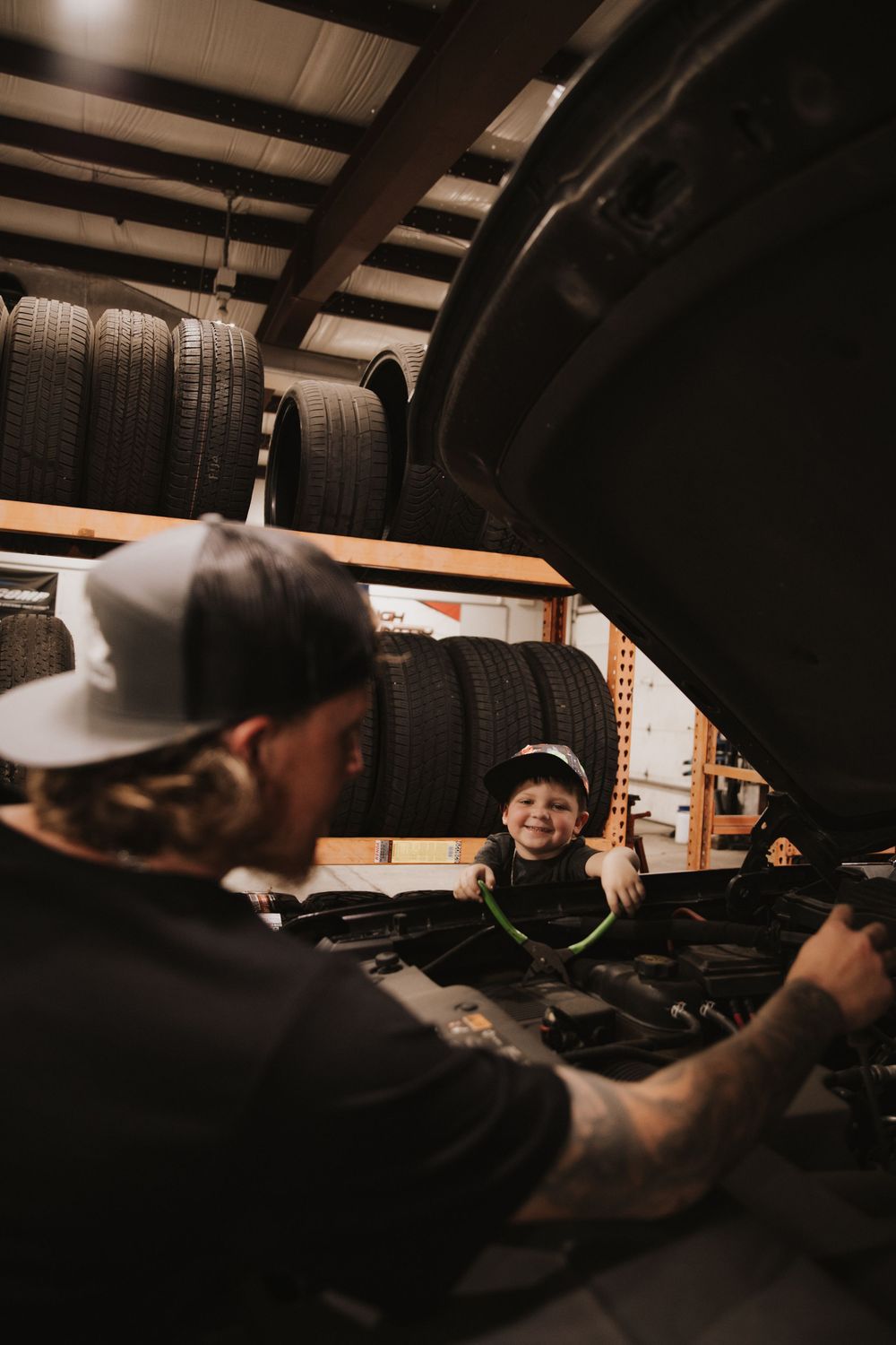 Workshop scene showing stored tires on shelves with figures working on vehicle maintenance in a dimly lit space.
