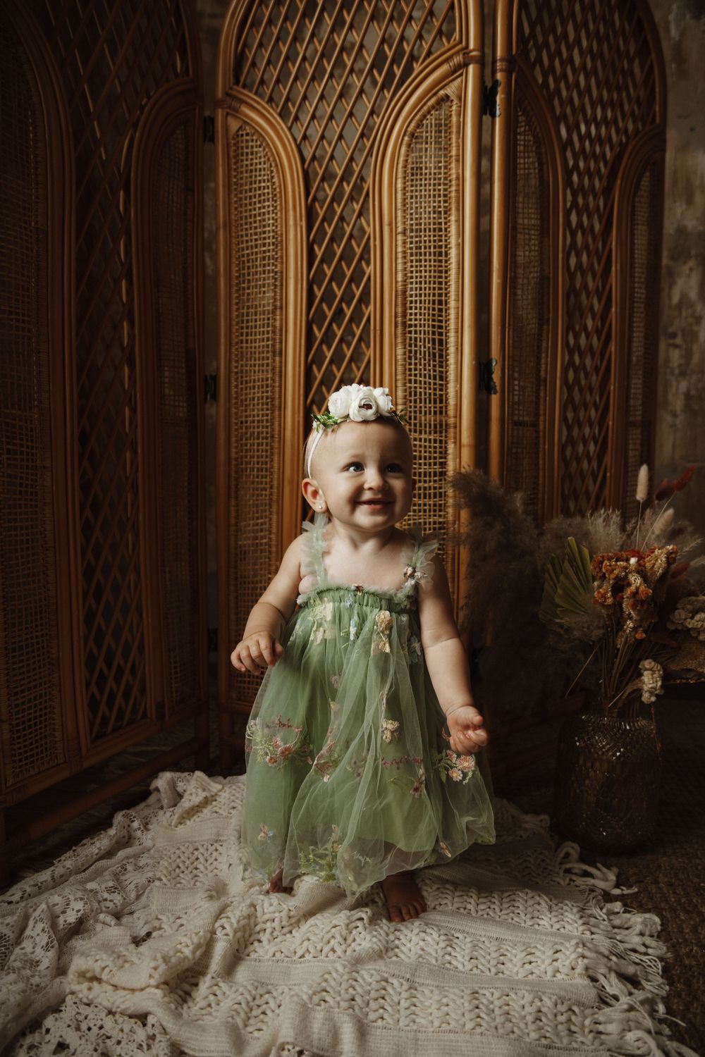 Small figure in a mint green dress stands before ornate wooden doors on white lace in vintage-style portrait setting.