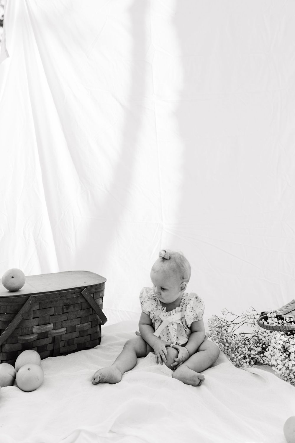 A series of black and white photos showing a baby sitting with a blanket against a white backdrop.