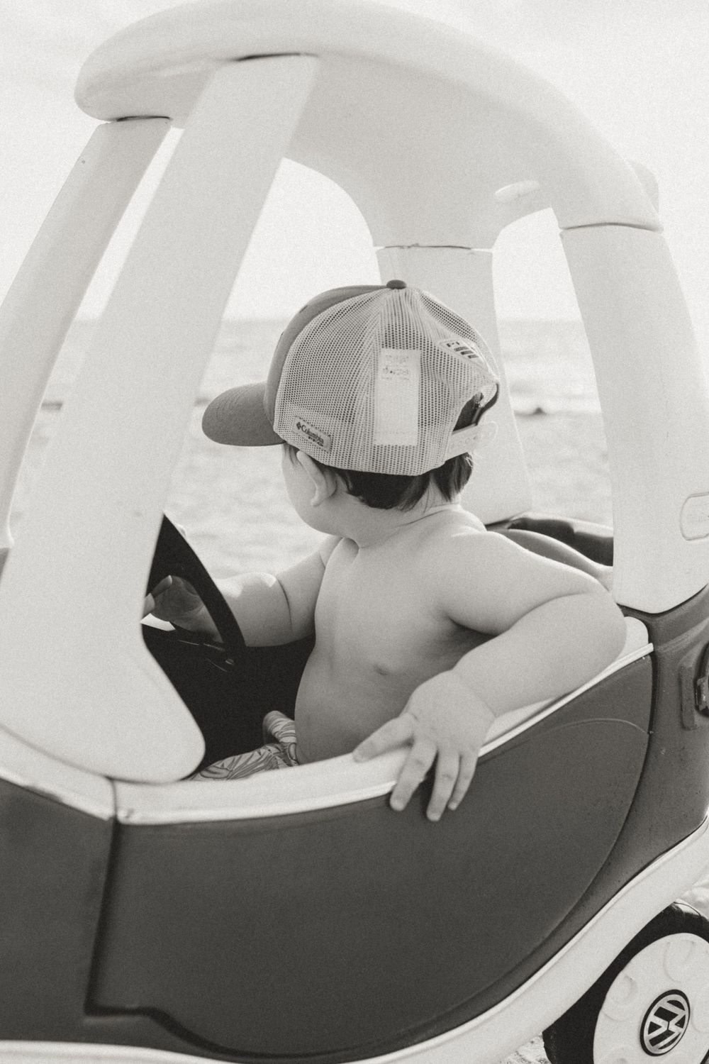 Black and white photo of child in vintage-style toy car outdoors.