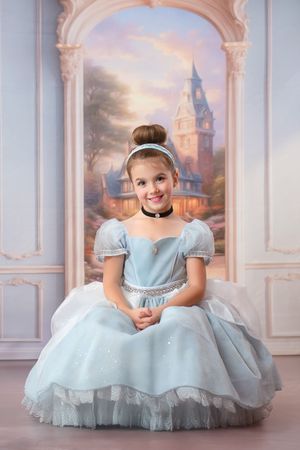 A magical portrait in front of an elegant archway and castle backdrop featuring a light blue princess-style ball gown and tulle.