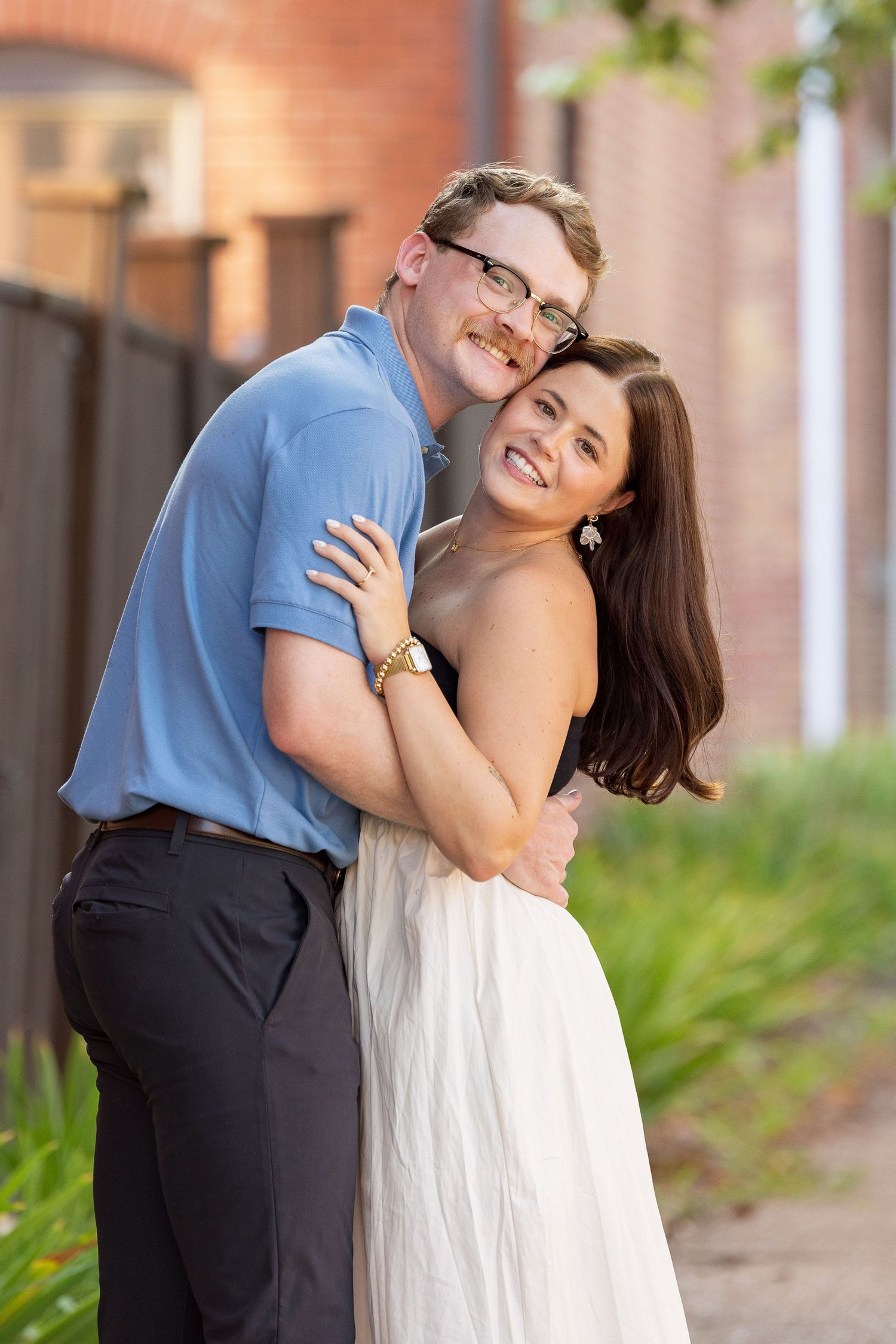 A bride and groom standing together under a large tree in a grassy outdoor setting.