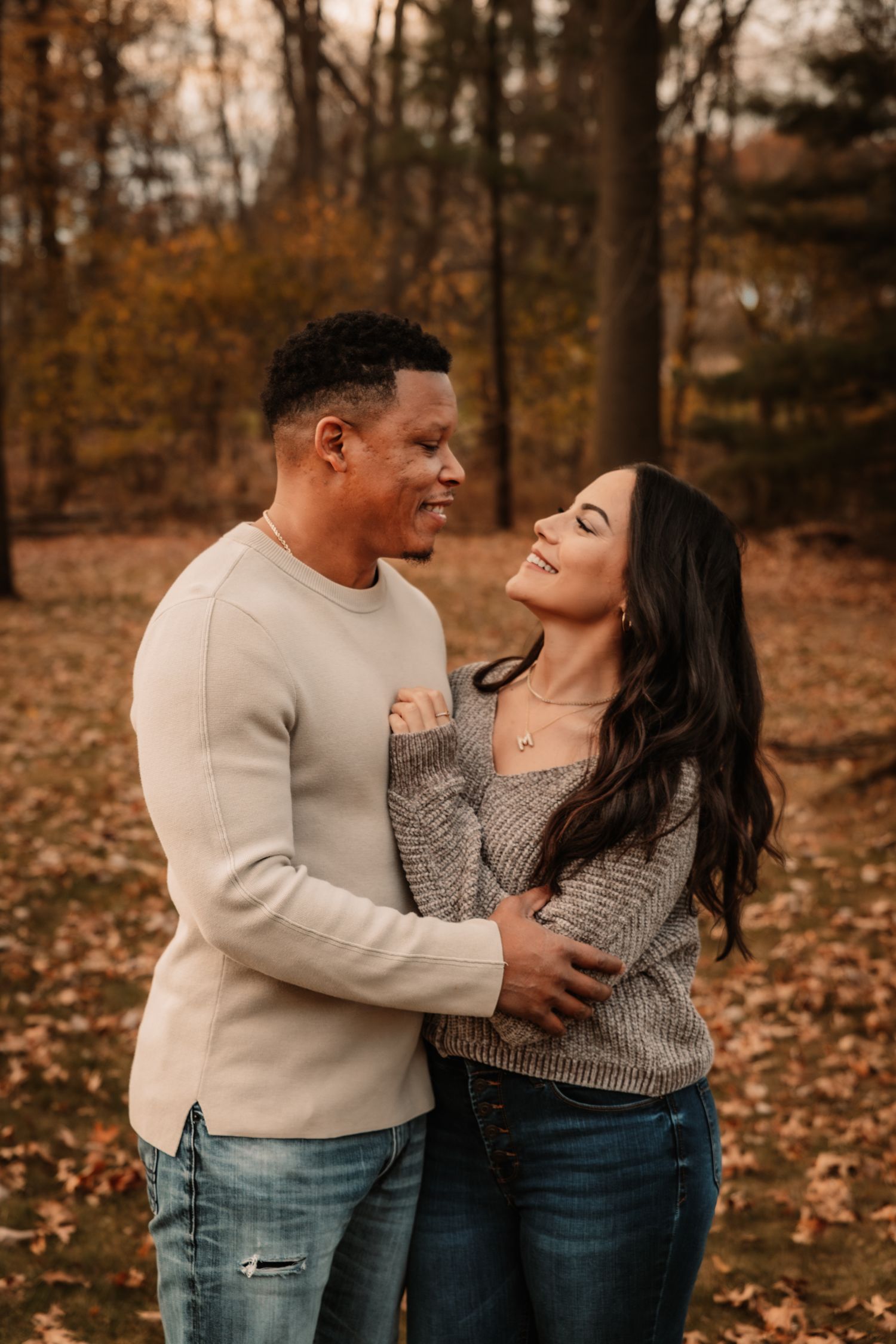 A couple shares a tender moment together on fallen autumn leaves in the woods.