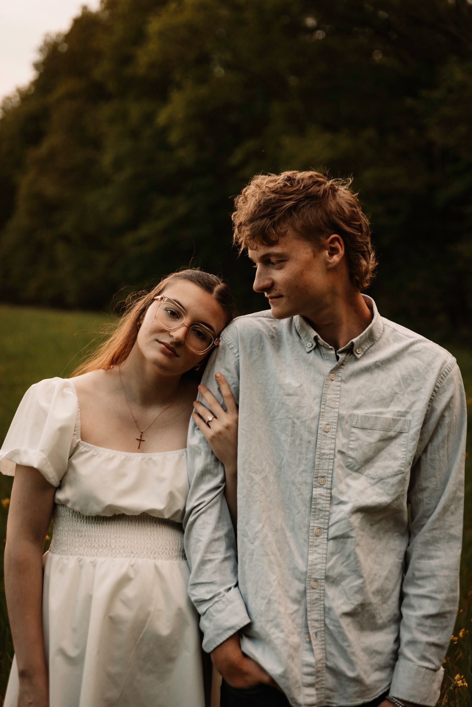 A romantic couple in casual attire embraces in a series of intimate outdoor portraits at sunset.