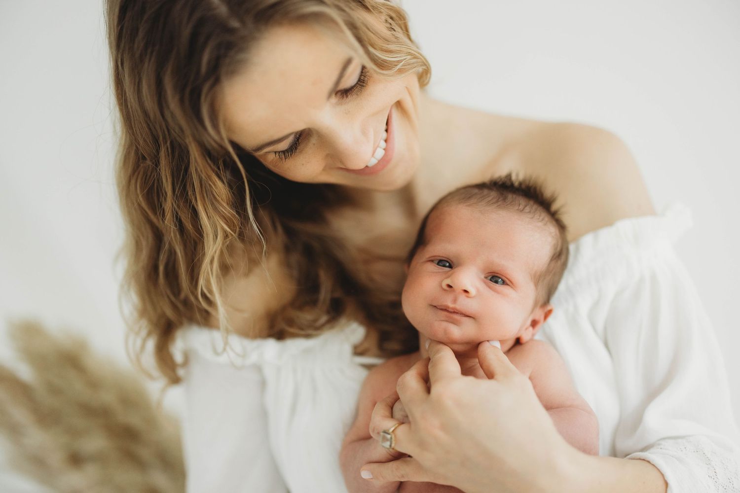 A tender moment between mother and newborn baby against a white background with soft natural lighting.