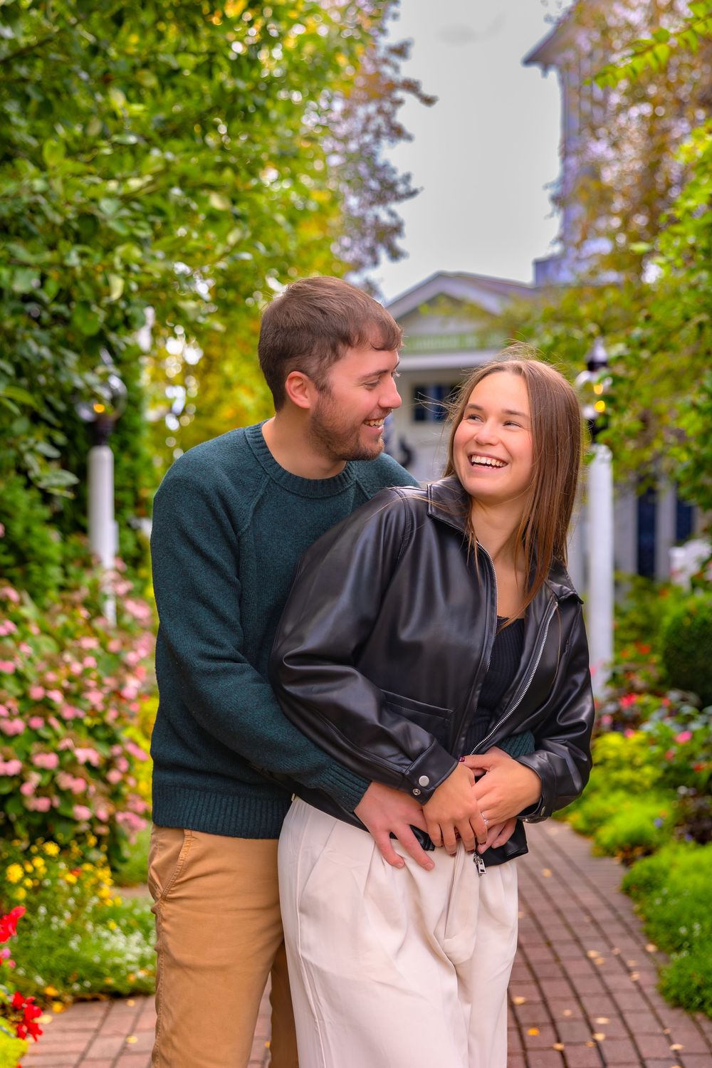 A couple shares a joyful moment together while walking through a garden path with colorful flowers and greenery.