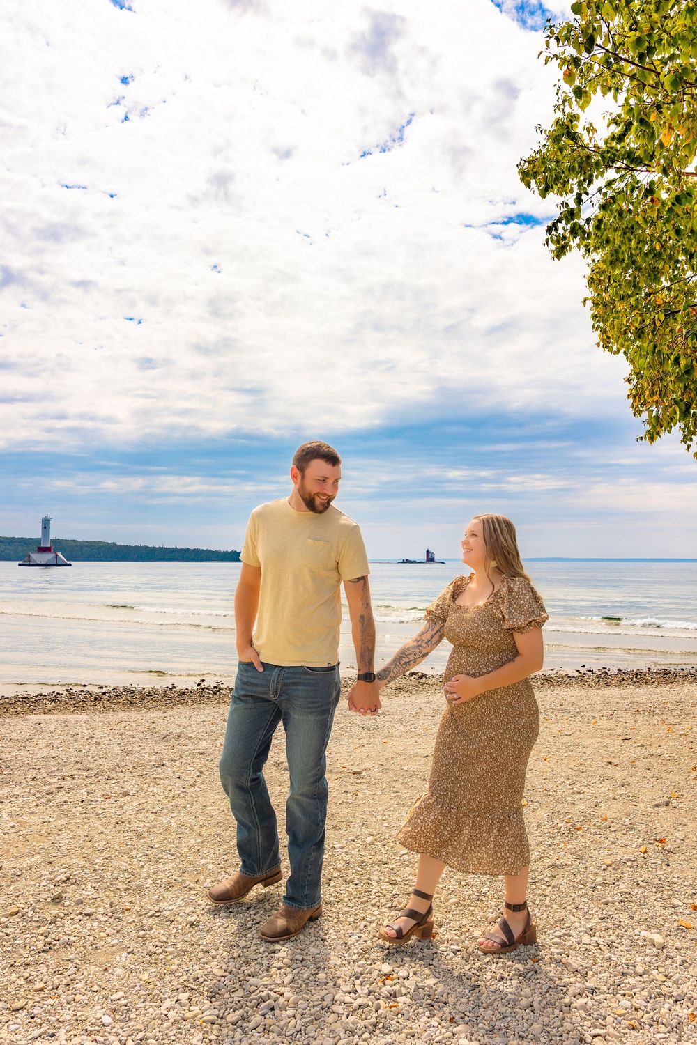 A couple walks hand in hand along a scenic beach shoreline on a sunny day with clouds overhead.