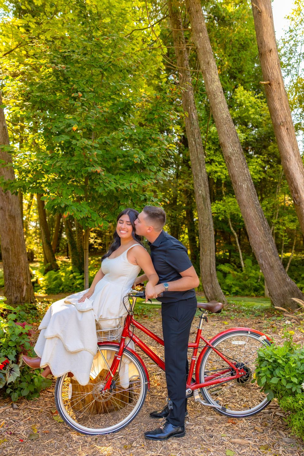 A romantic wedding photo series showing a couple with a vintage red bicycle in a wooded outdoor setting.